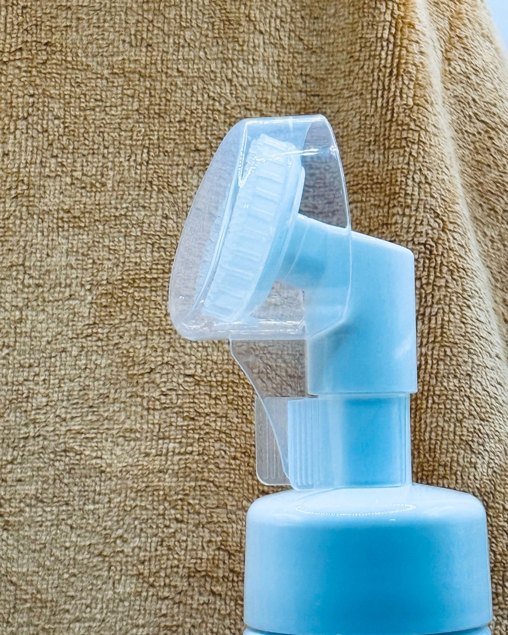 Blue spray bottle with transparent nozzle against a textured beige background